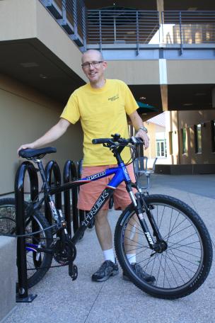 Professor Todd Heible poses with his bicycle in front of the bike rack outside the PS building