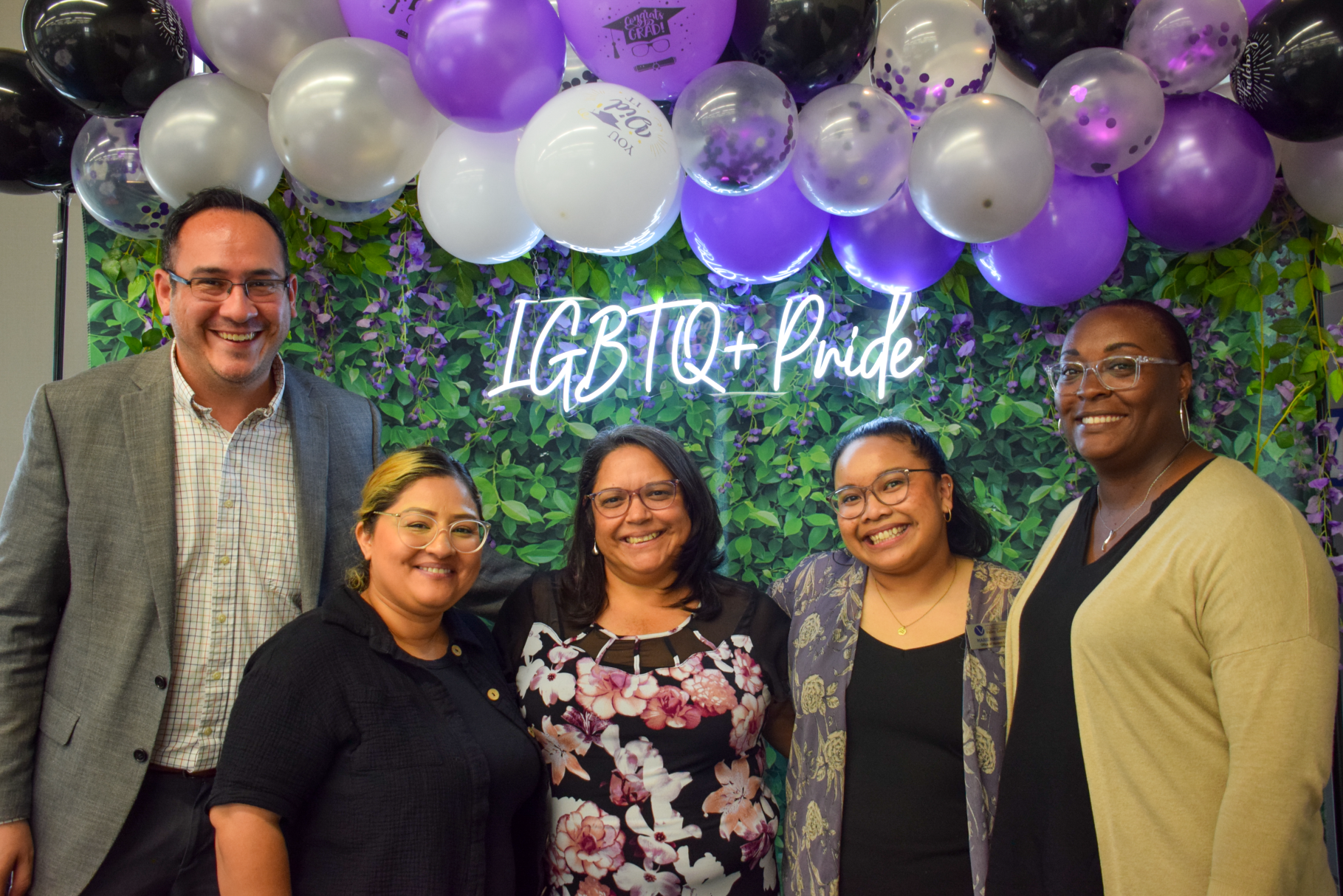 A group photo of faculty in front of some balloons and a LGBTQ+ Pride neon sign