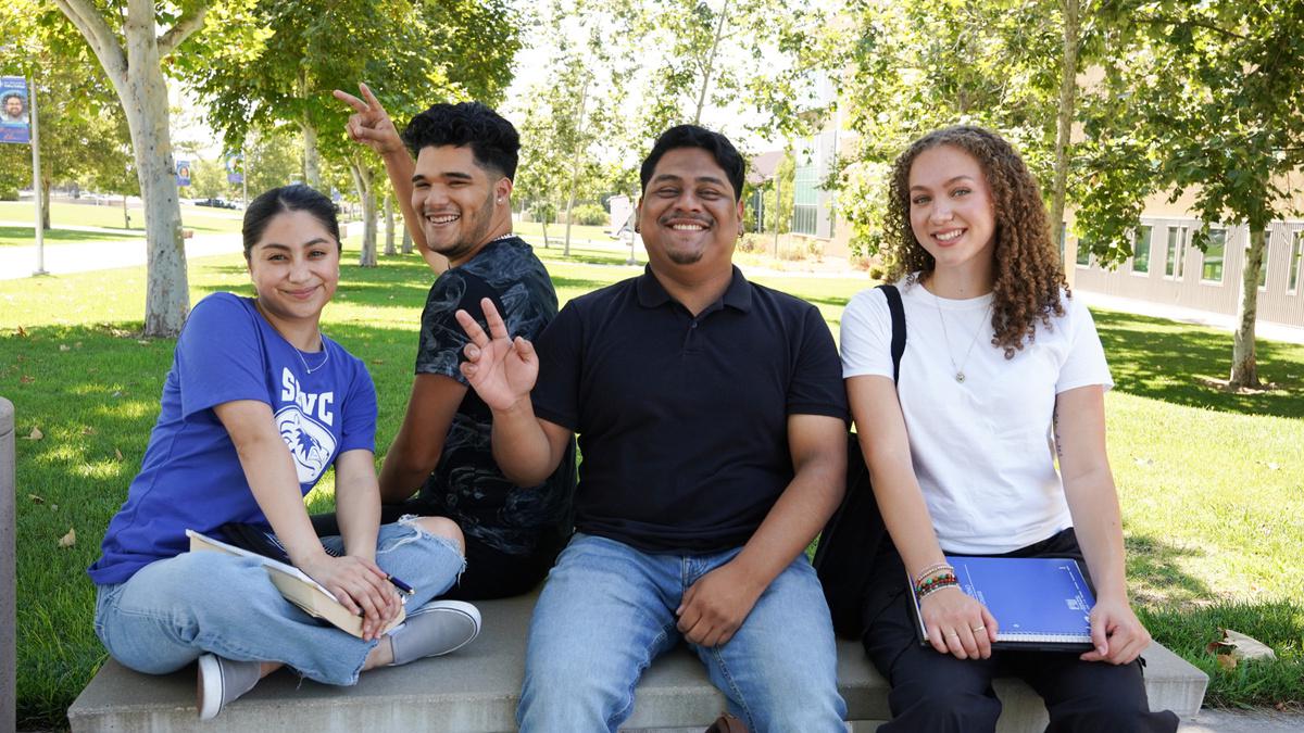 4 students sitting on a bench outside on SBVC campus smiling