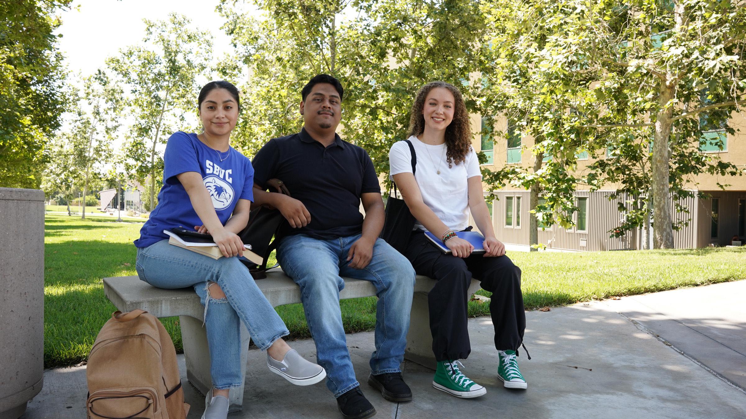 Three students sitting on a bench smiling