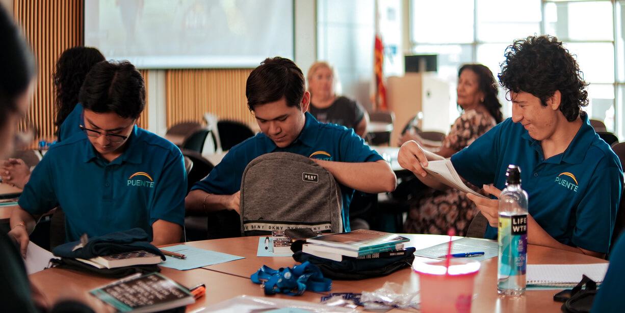 Three first-generation students sitting at a table with embroidered "Puente" polos