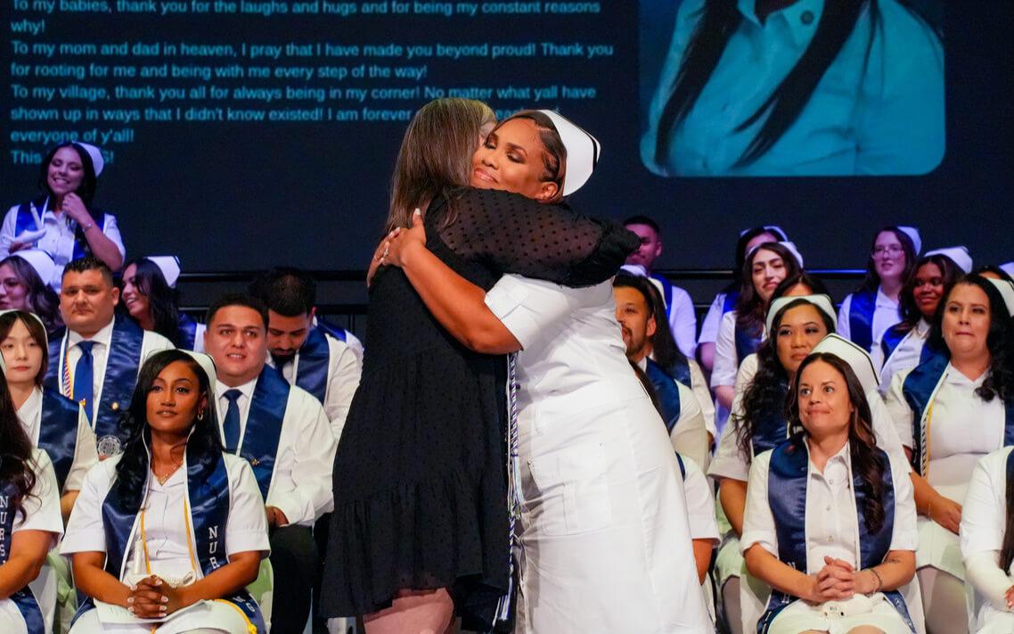 A nursing graduate embraces an instructor on stage