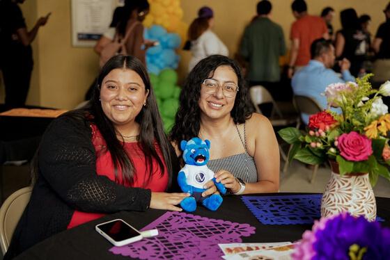 Two students smiling and holding a Blue the Wolverine plushie