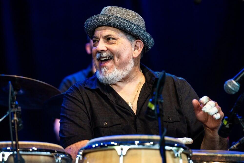 Poncho Sanchez smiling and playing the bongos