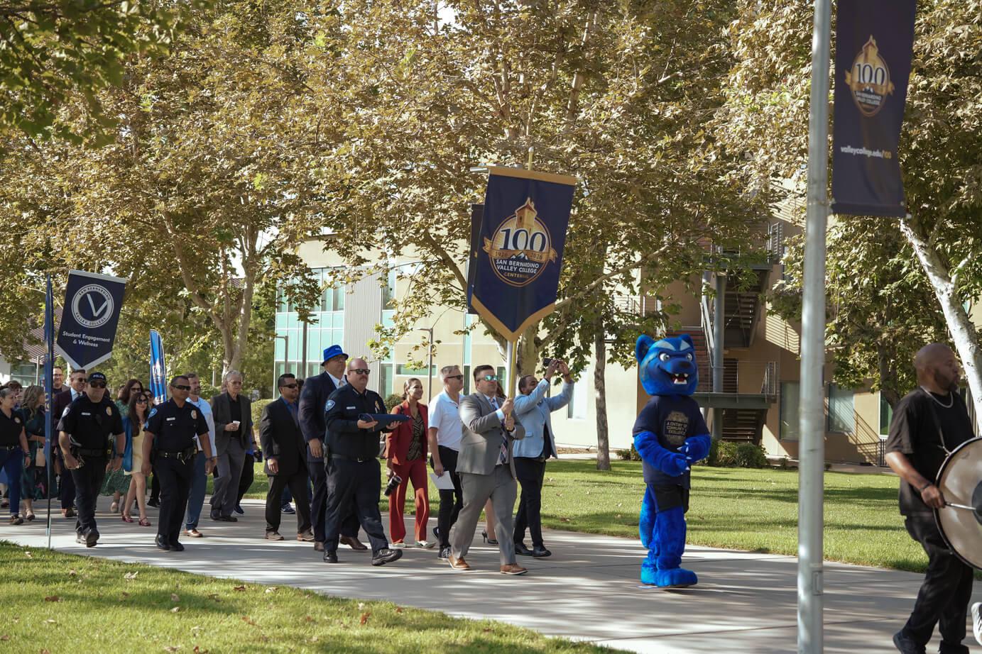 A procession of faculty & staff following Blue the Wolverine
