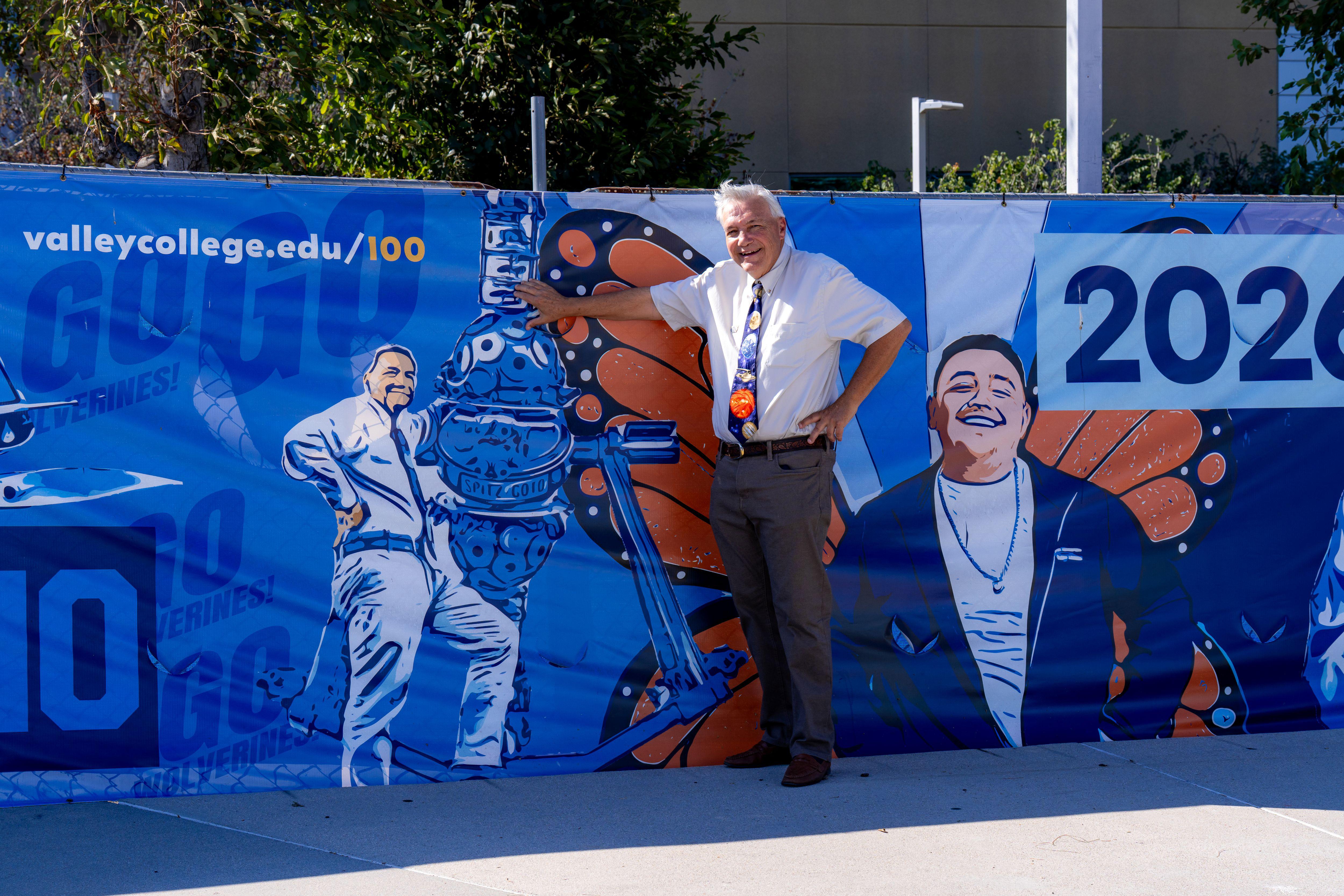 Man stands in a front of a blue fence banner depicting him with astronomy equipment