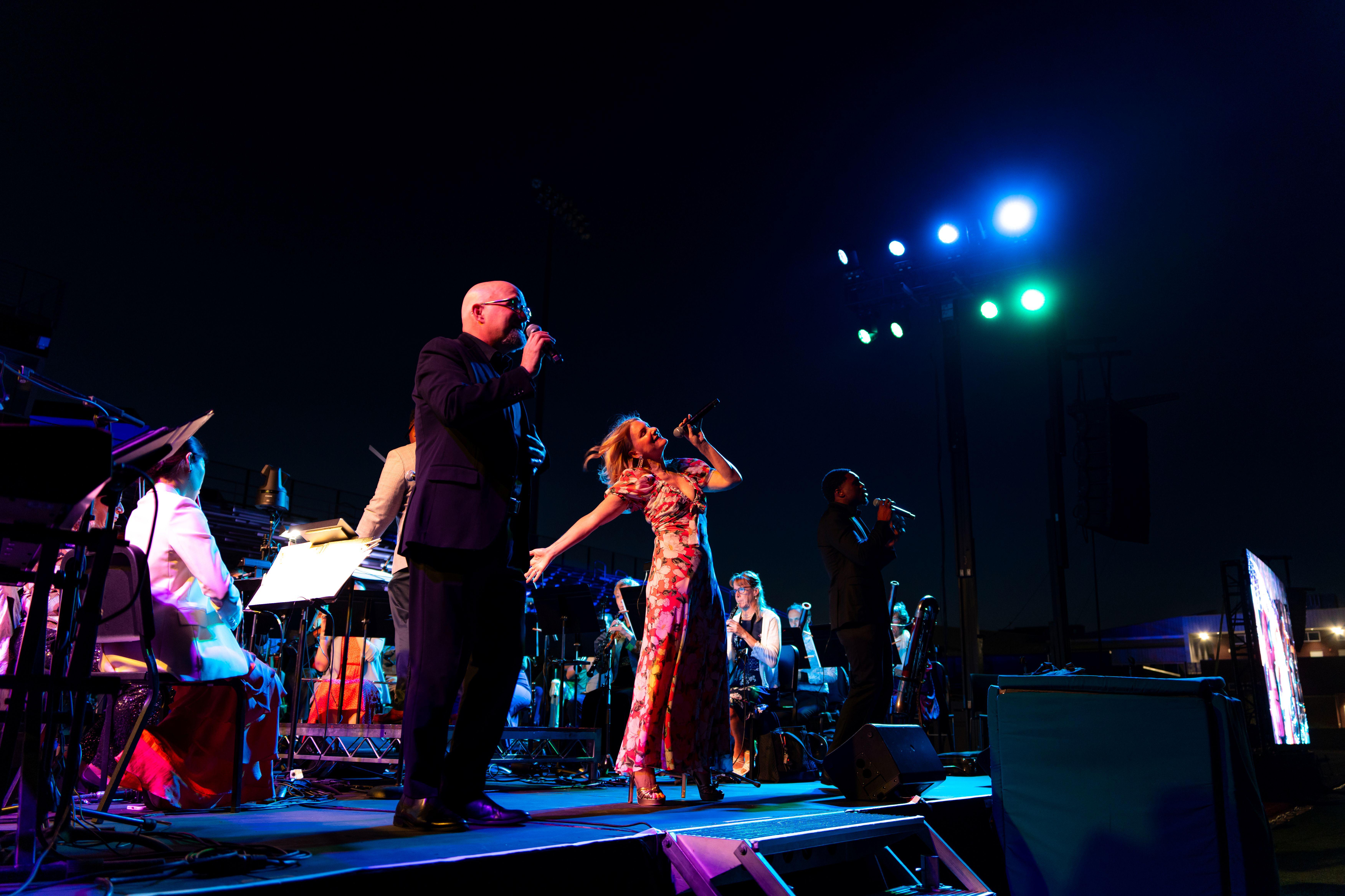 Performers sing on stage with a symphony playing behind them