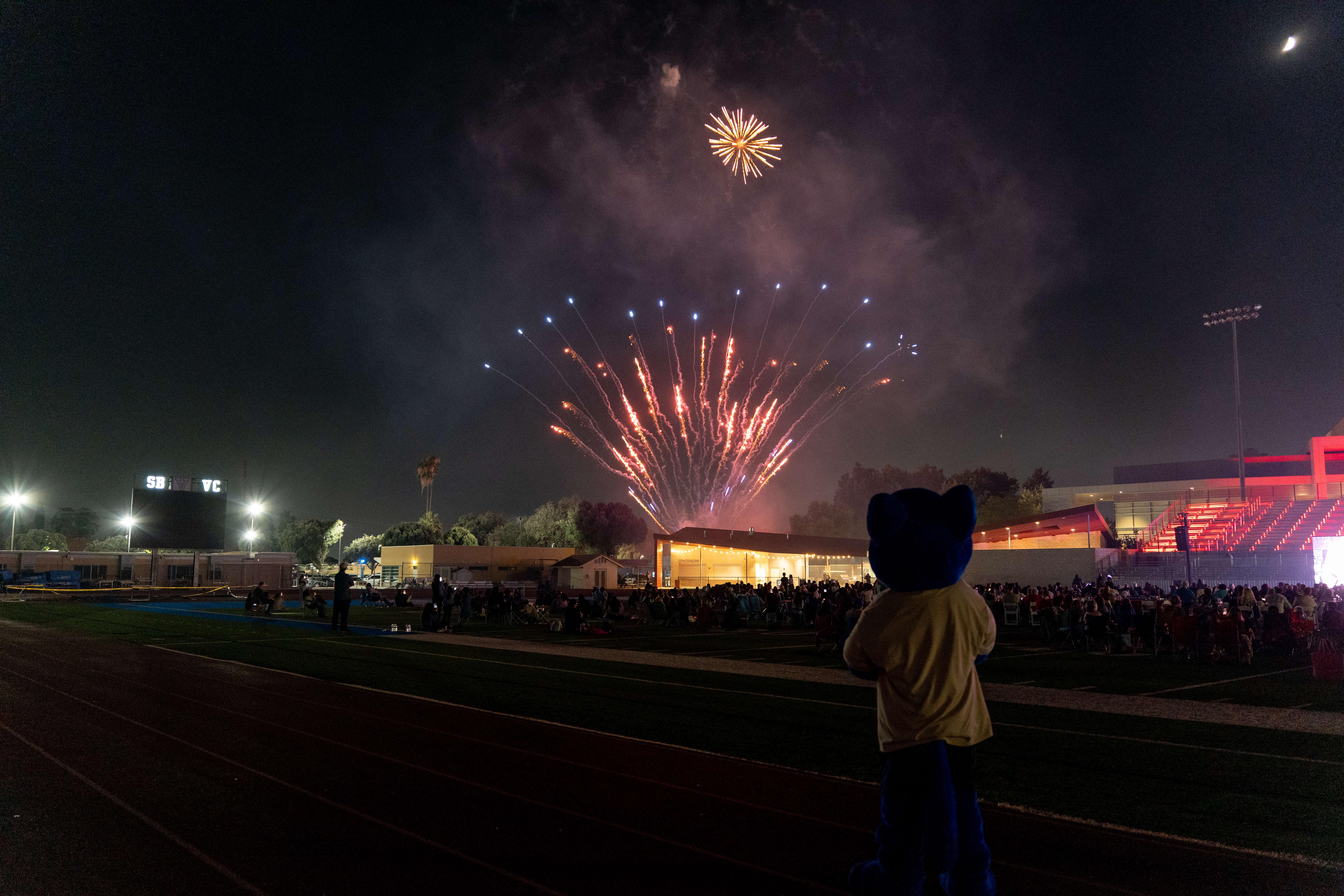 Fireworks are shot off with SBVC mascot Blue raising his arms in the foreground