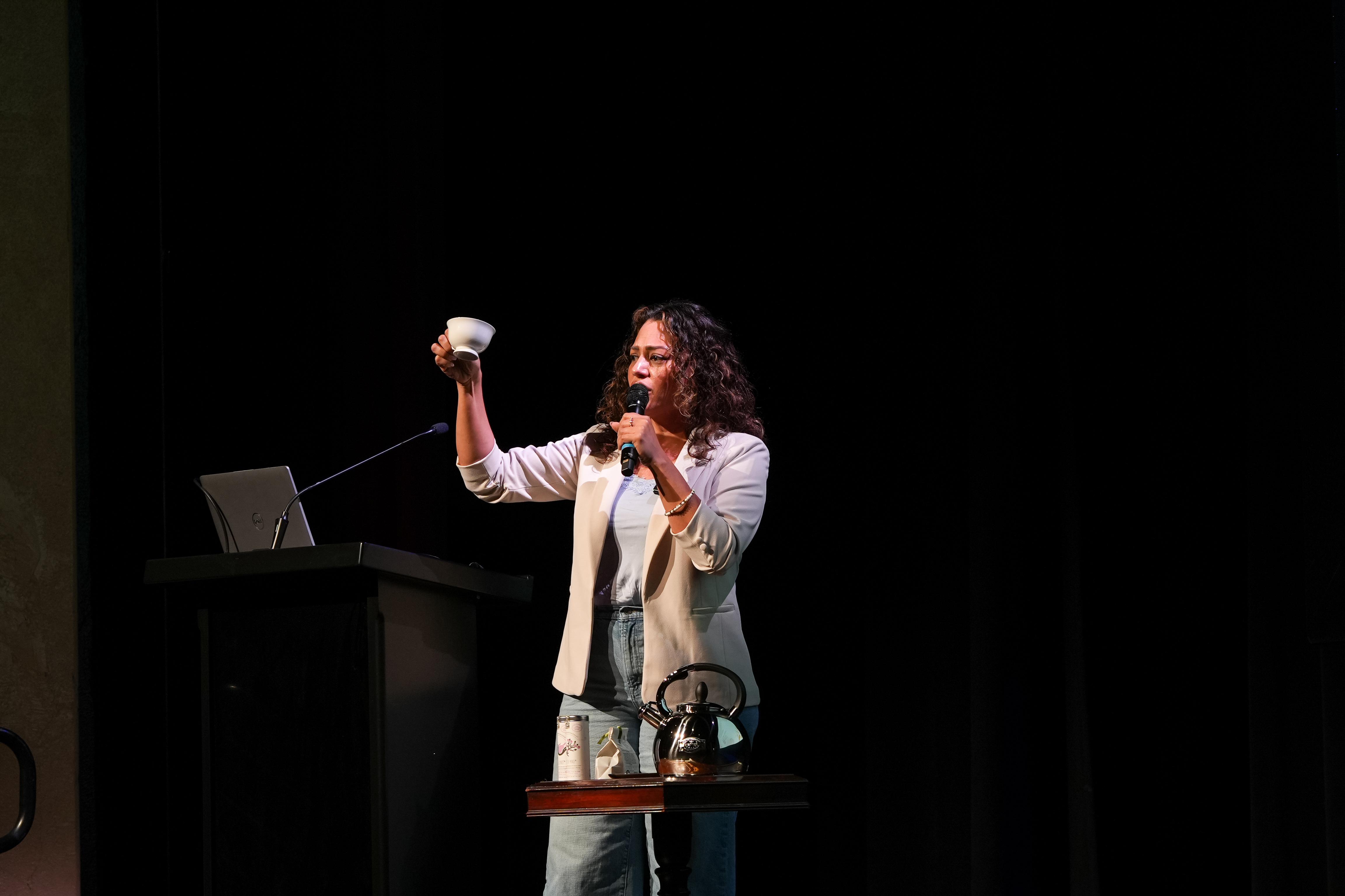 A woman holds a cup of tea while speaking