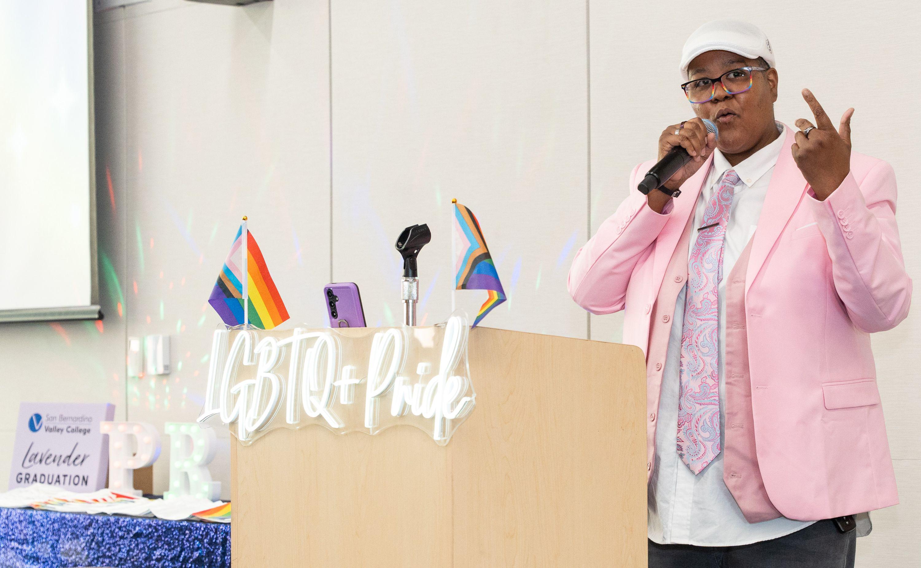 Woman in a pink coat speaks at Lavender Grad.