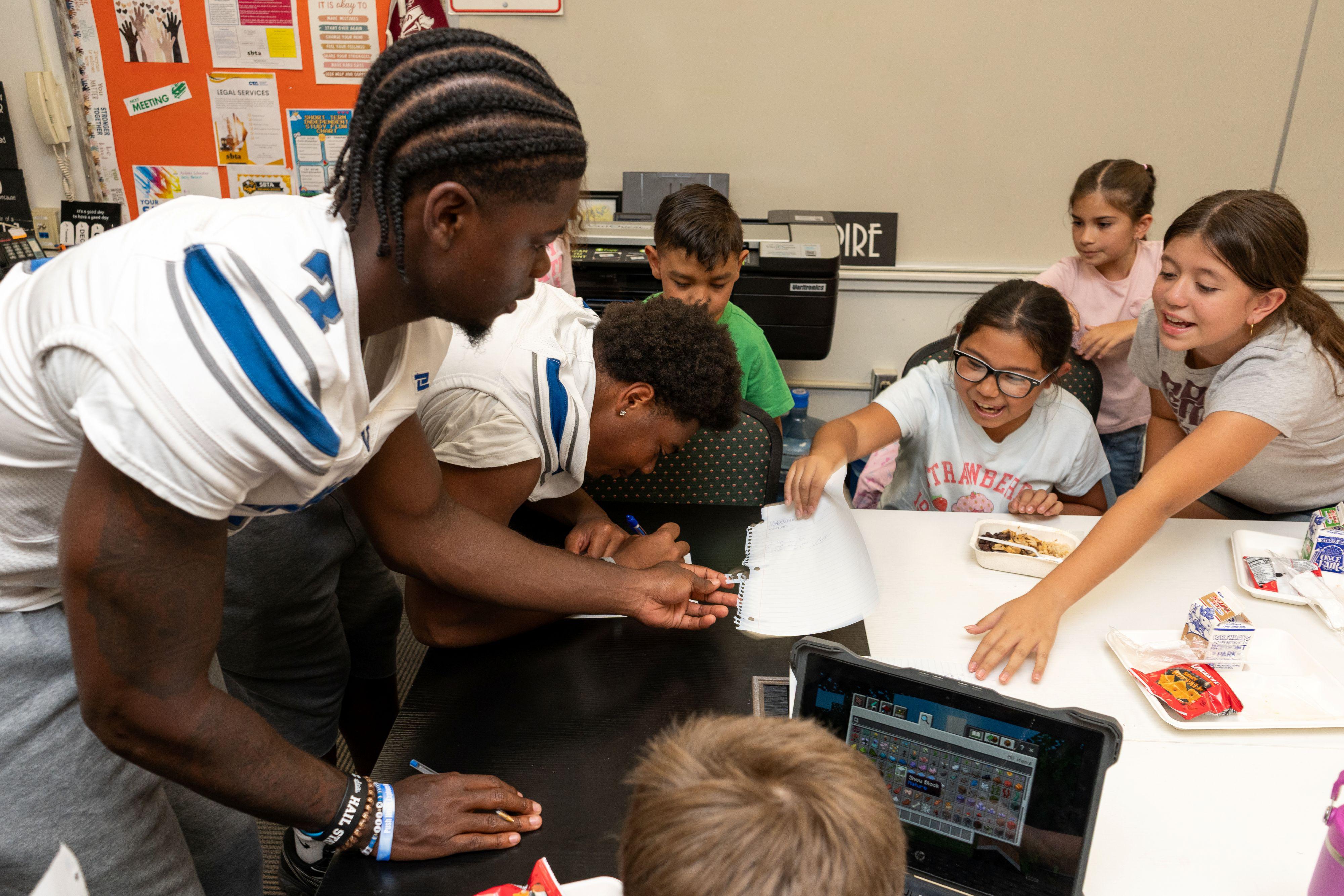 Two football players interact with elementary school children in classroom