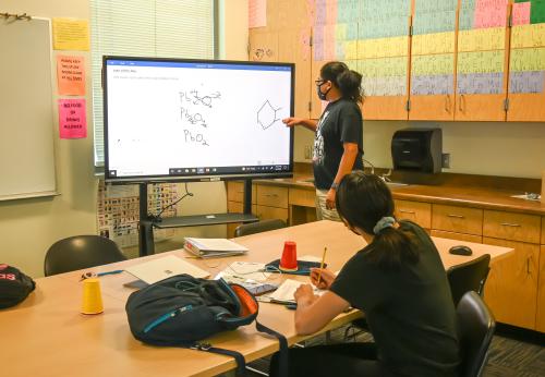 A teacher teaches in front of a digital screen.