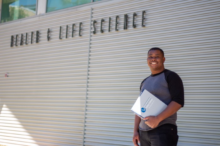 male student smiles in front of health science building